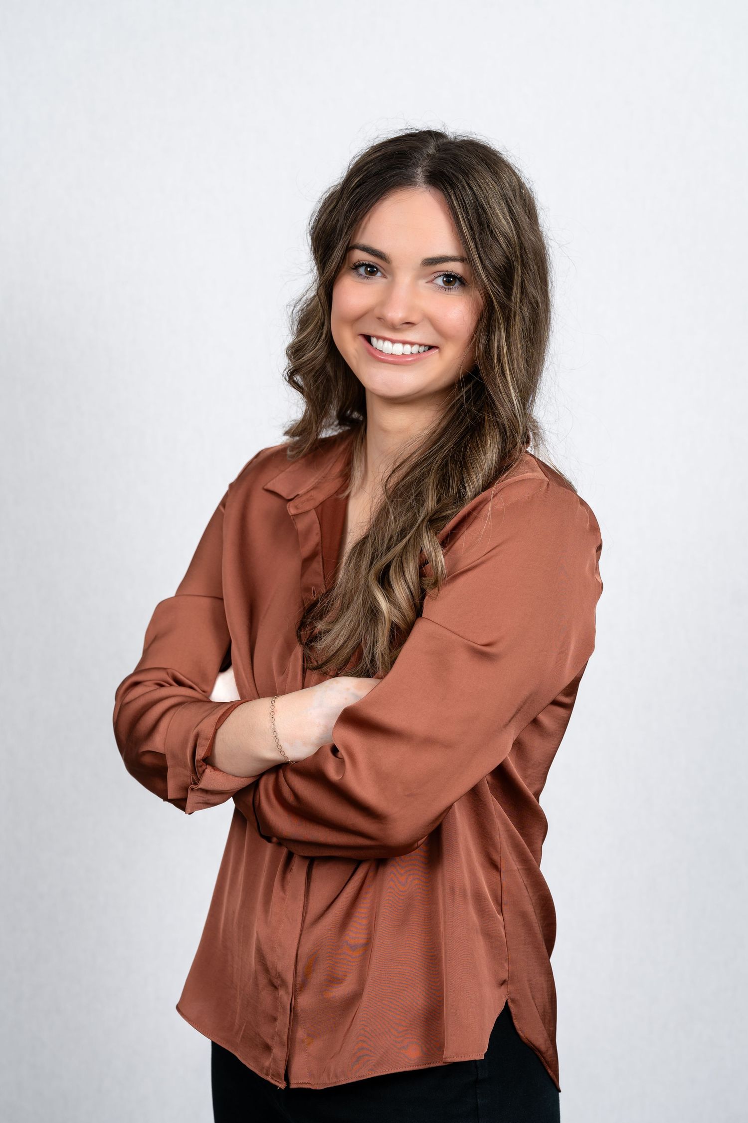 Portrait of a person in terracotta blouse with long wavy hair against white backdrop.