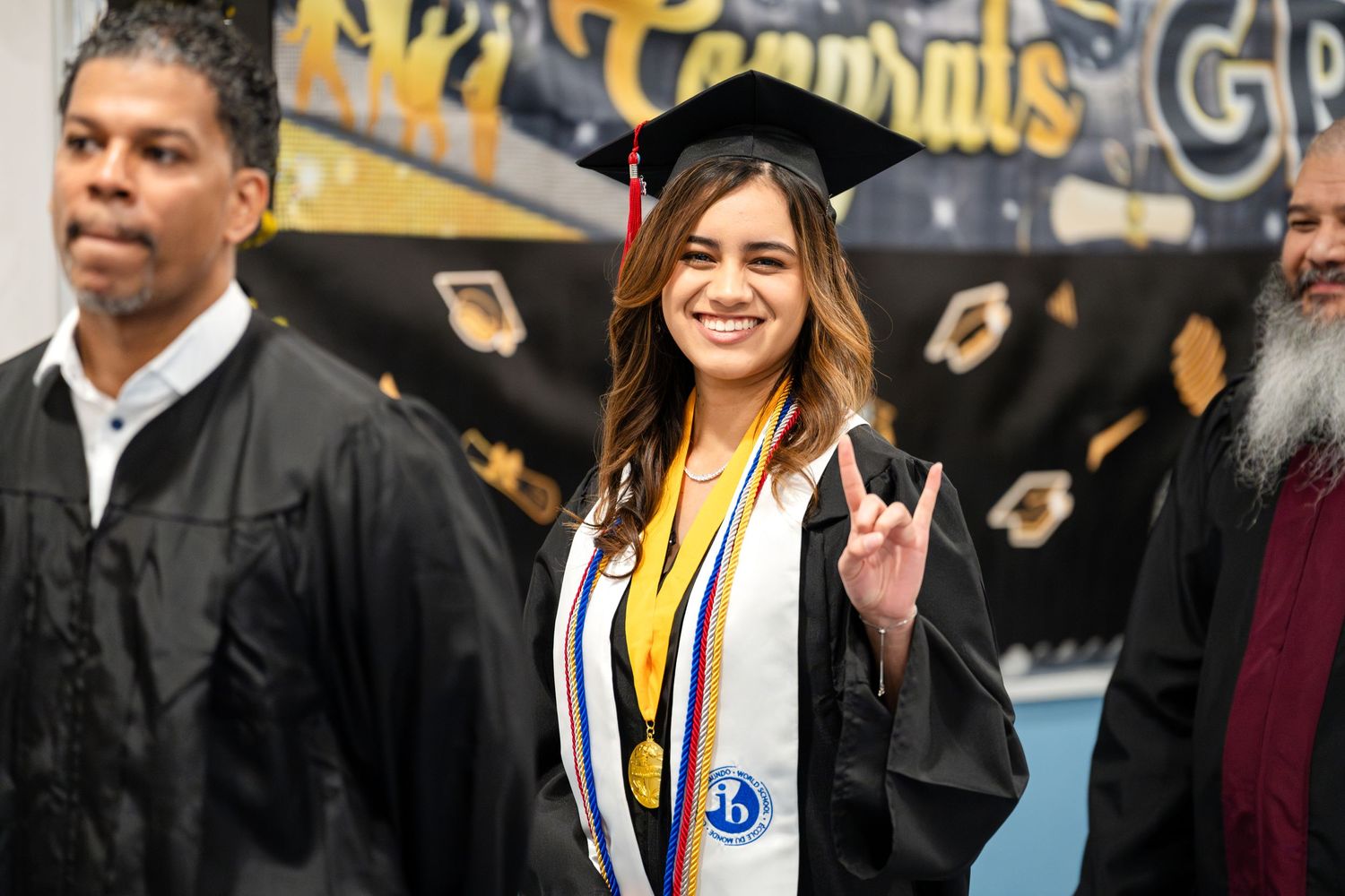 Graduate in black cap and gown flashes peace sign during celebration.