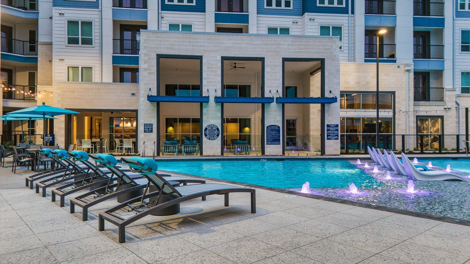 Modern pool deck with gray lounge chairs and colorful lighting features at an upscale apartment complex.