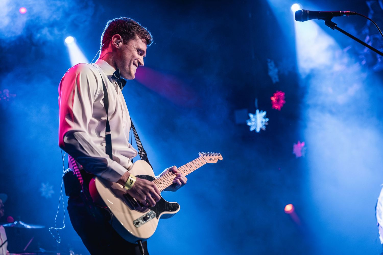 Concert guitarist performs passionately on stage with blue lighting and smoke effects.