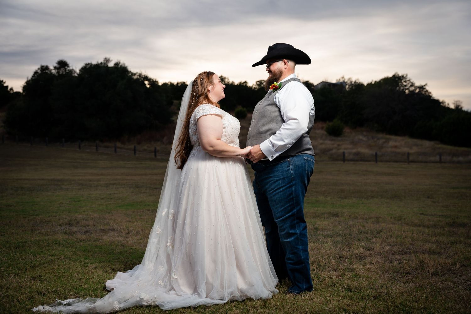 Sunset wedding portrait of couple in western attire standing in an open field.