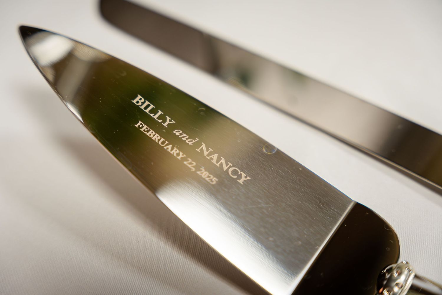 Close-up macro shot of a shiny stainless steel Bill and Nancy knife blade with engraved text.