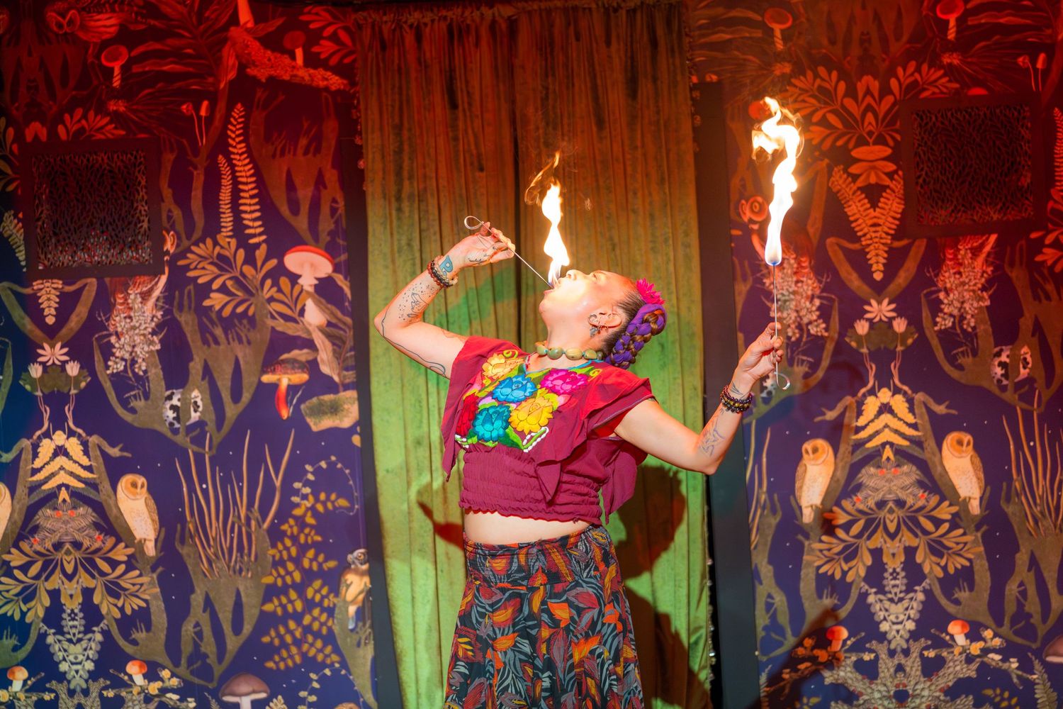 A performer in colorful attire does a fire dance routine against a decorative background.