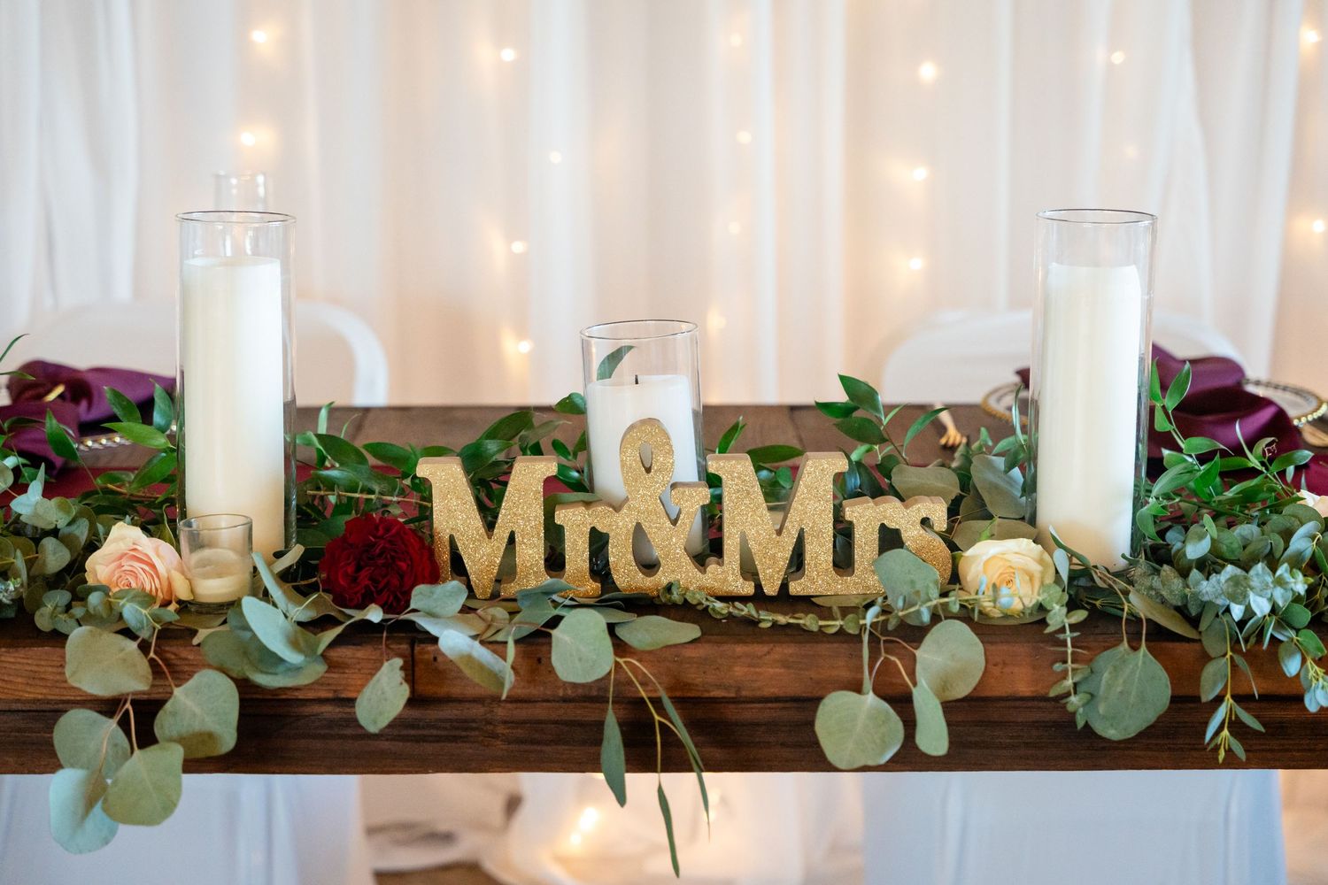 Wedding table decor featuring Mr & Mrs sign, candles, and eucalyptus garland.