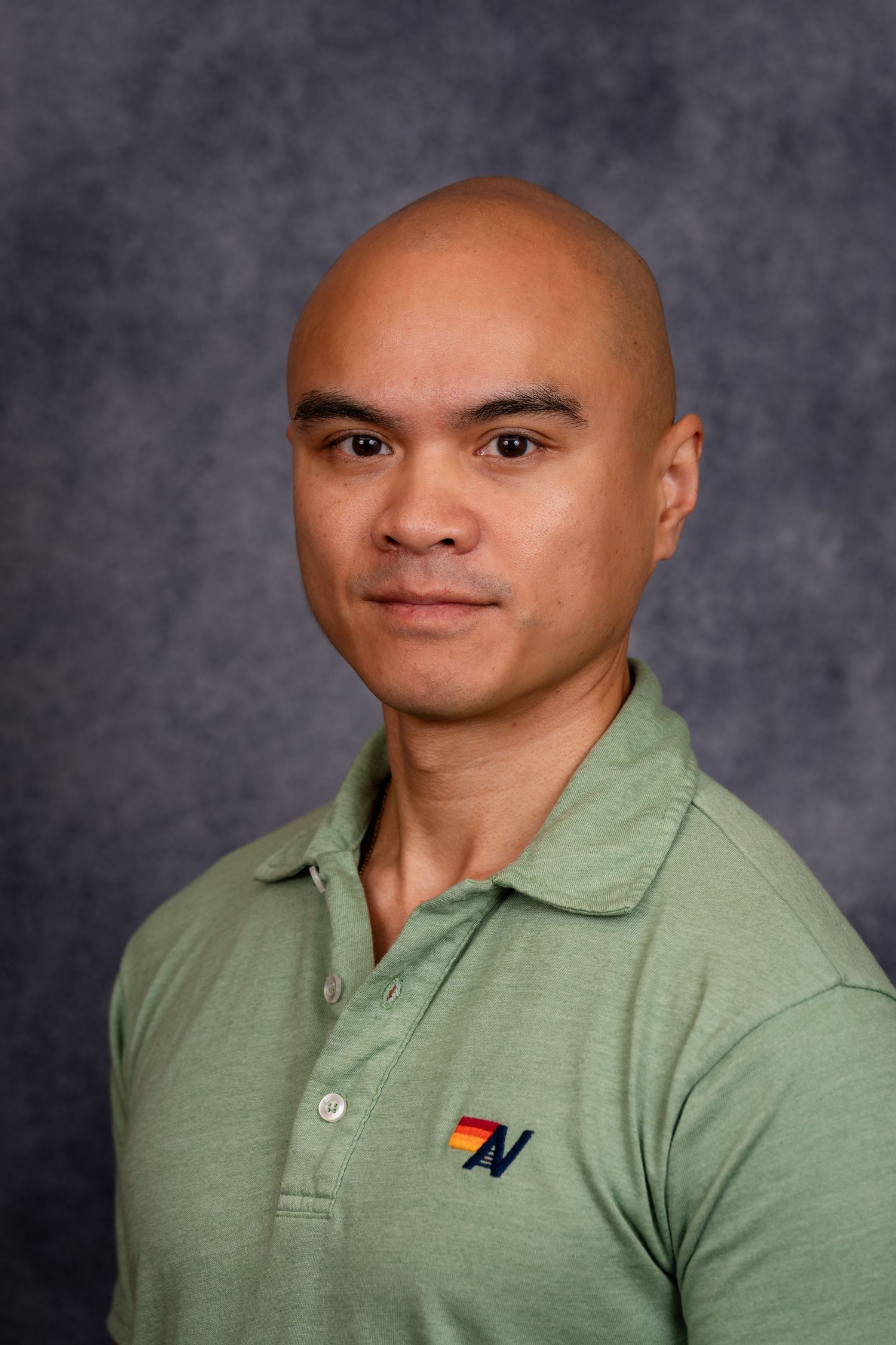 Professional headshot of person wearing green polo with company logo against gray background.