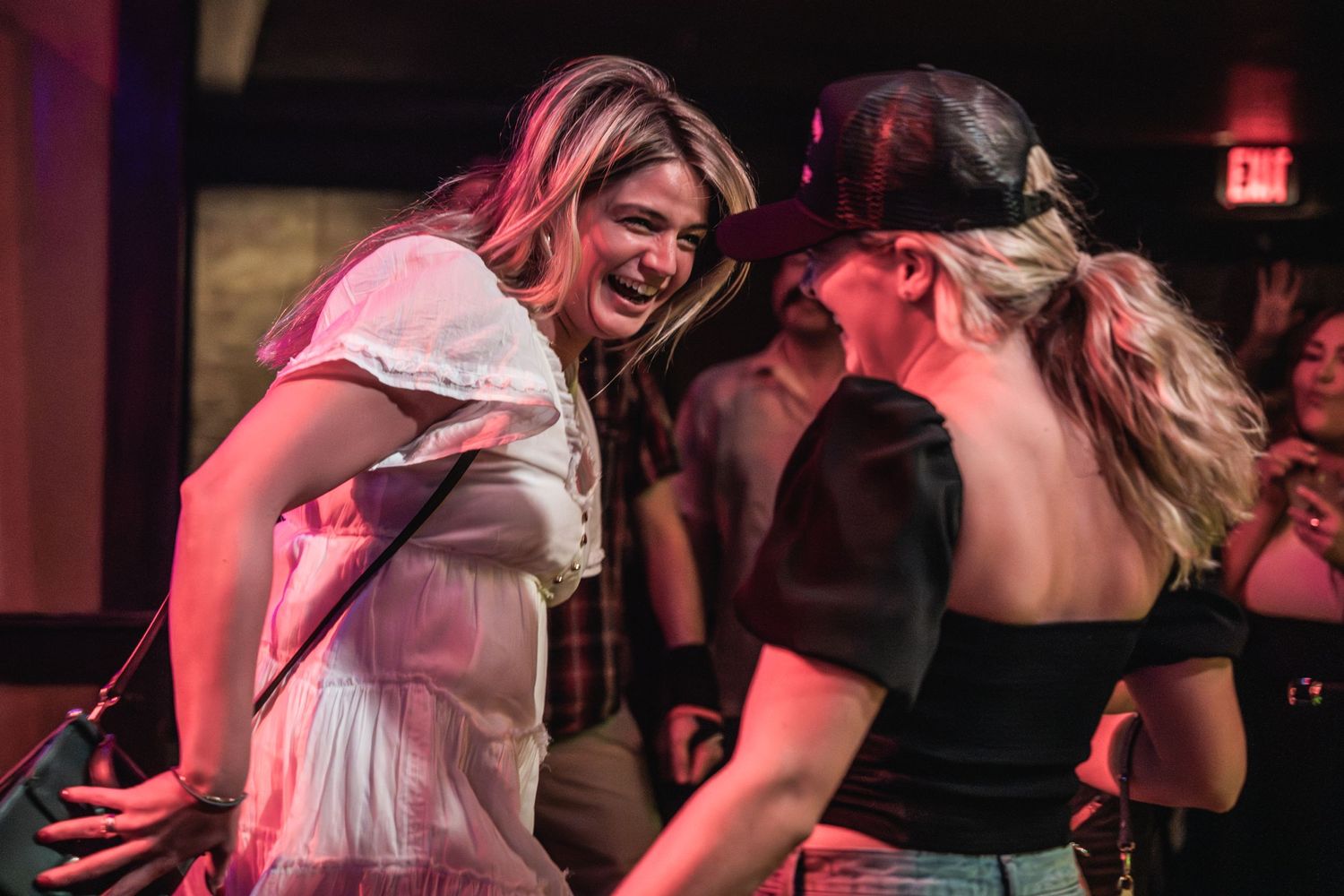 Concert attendees dance enthusiastically under red stage lighting at a live music venue.