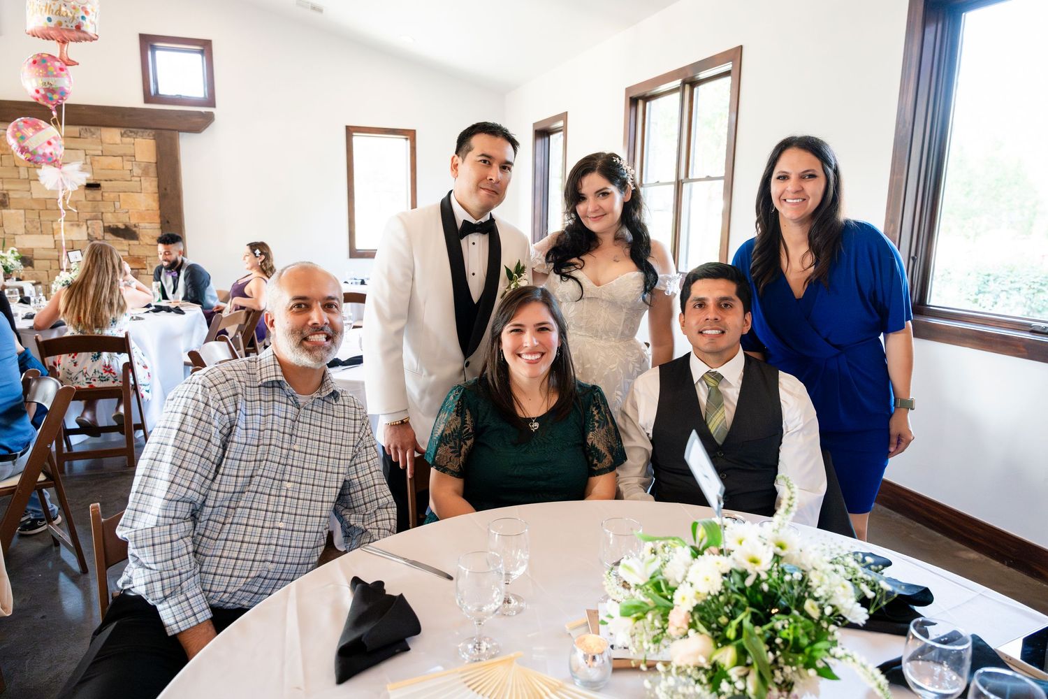A group of people seated and standing at a round table decorated with white flowers at an elegant event venue.