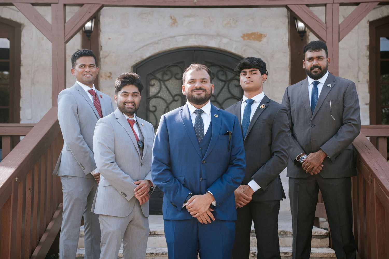 Groomsmen in coordinated suits posing together on rustic porch steps.