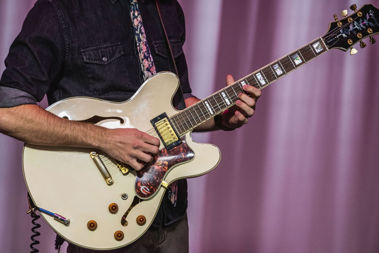 Close-up of musician playing white electric guitar against pink curtain.