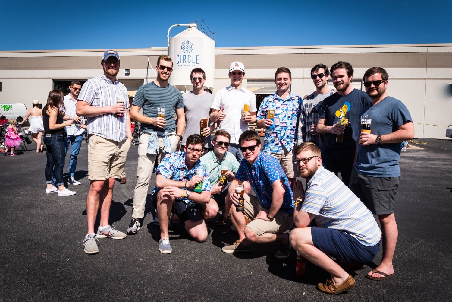 A group of brewery visitors pose together outside Circle Brewing Company on a sunny day.
