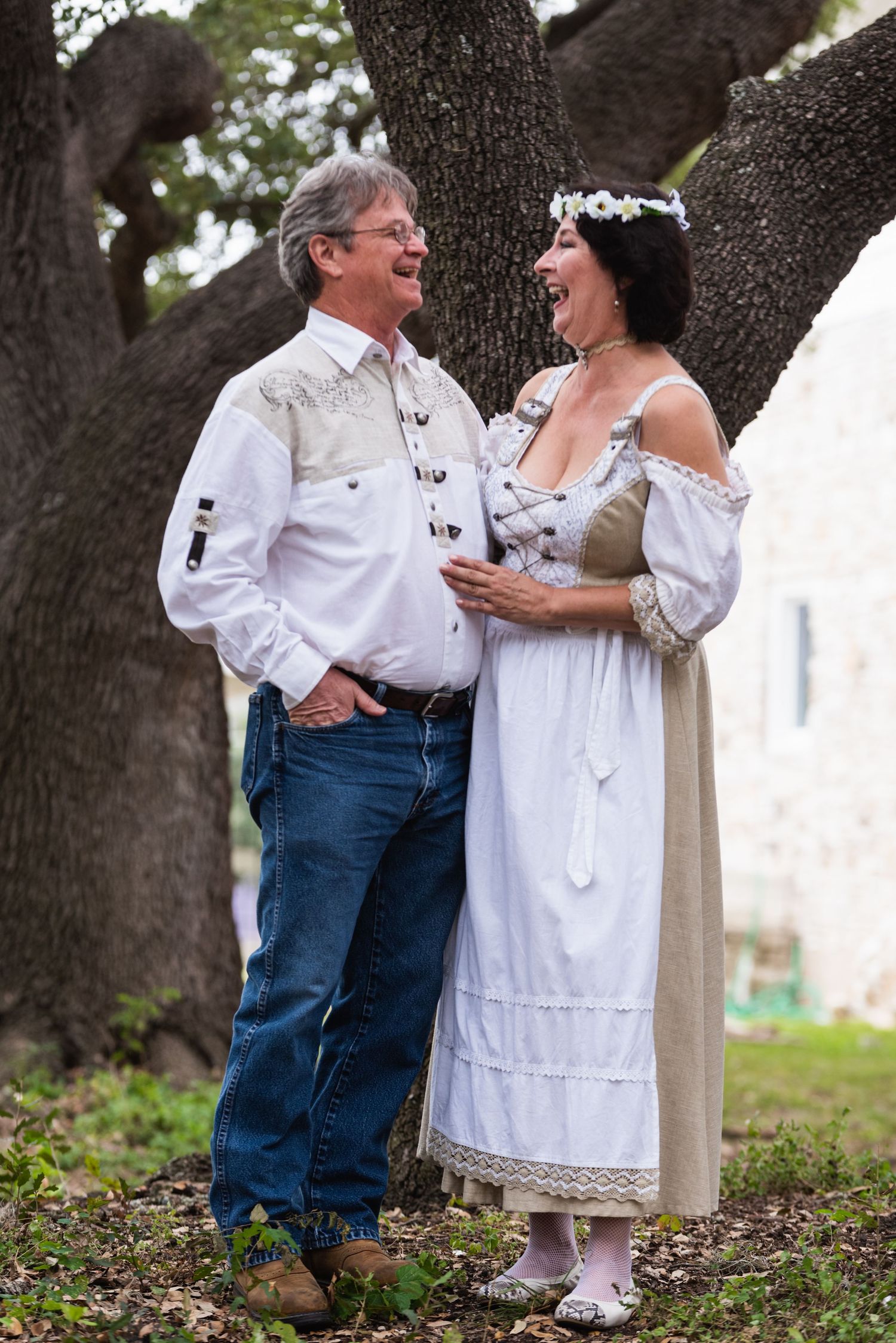 A couple shares a romantic moment under large oak trees, dressed in vintage-inspired attire.