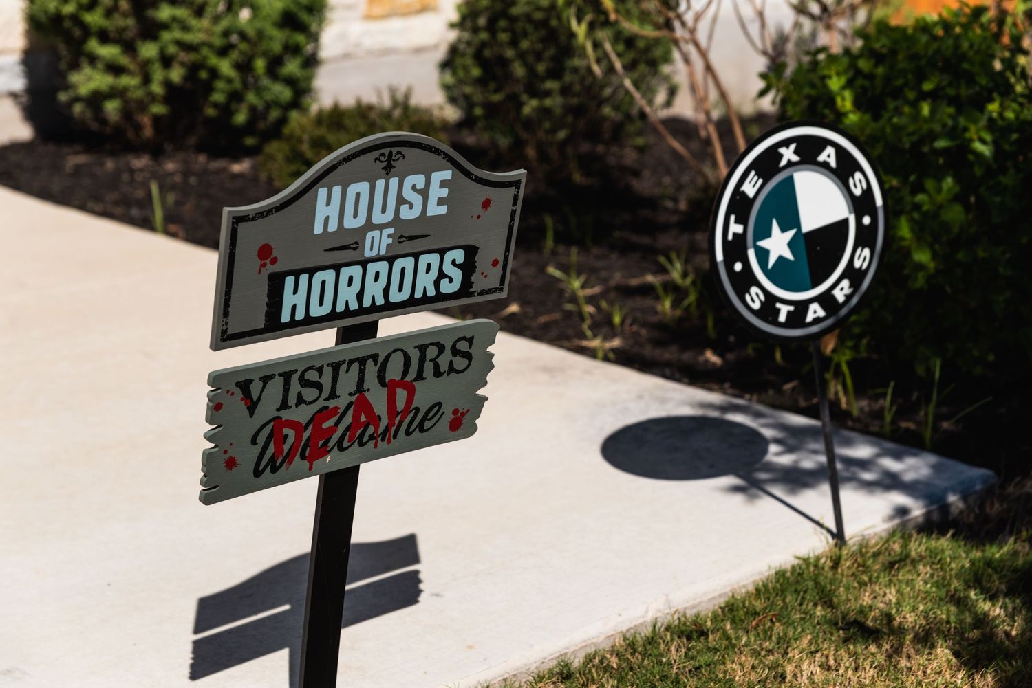 A spooky 'House of Horrors' sign posted in a garden setting.