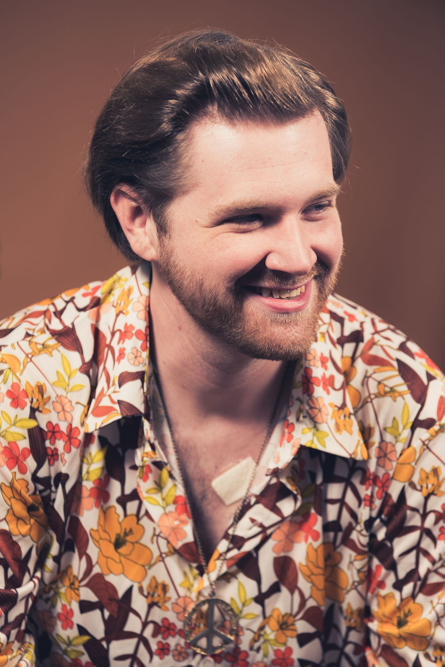 Person wearing orange and brown floral shirt smiles warmly in studio portrait.