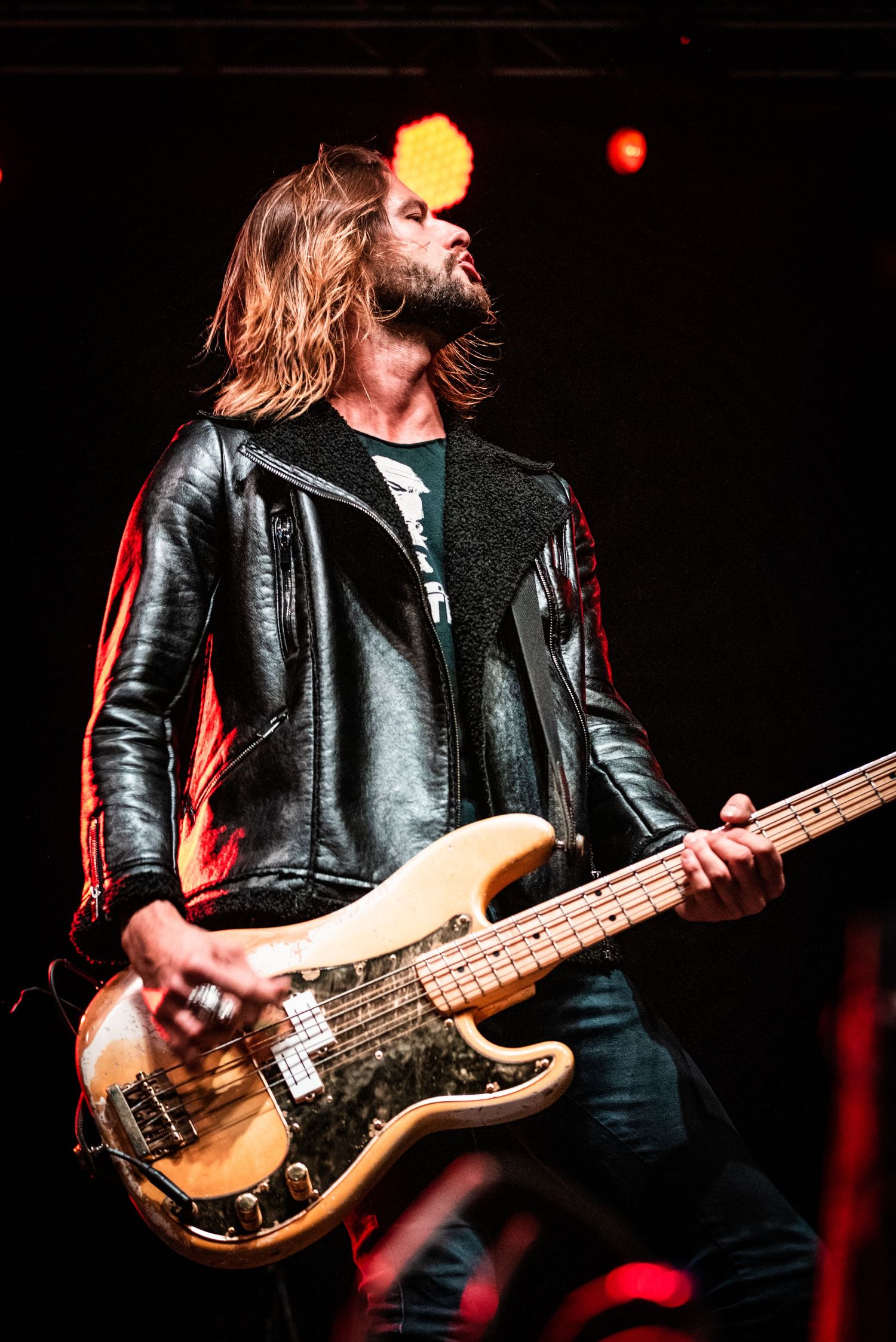 Rock bassist in leather jacket playing vintage bass guitar under stage lights.