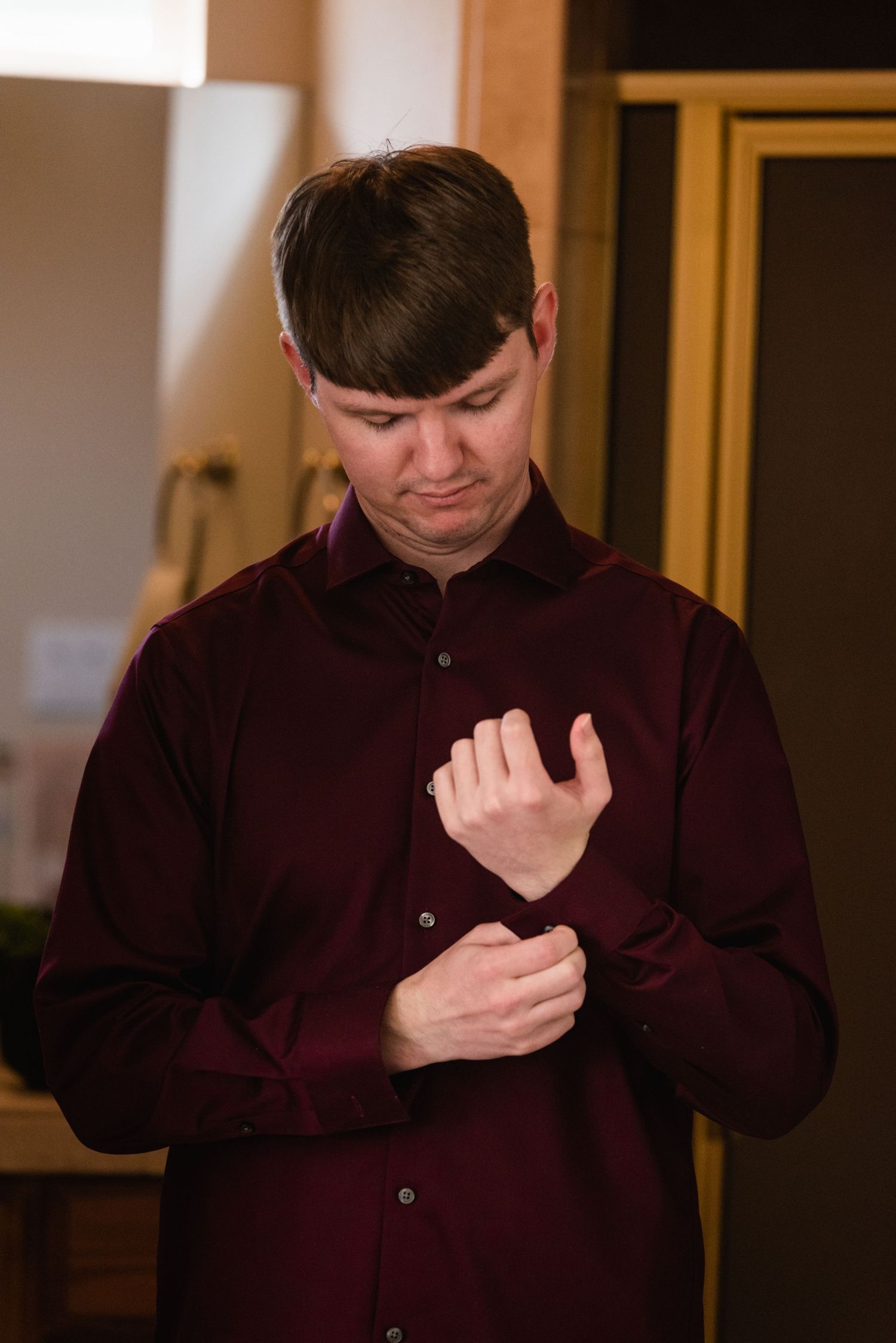 Person in burgundy shirt adjusting cuffs during wedding preparation.
