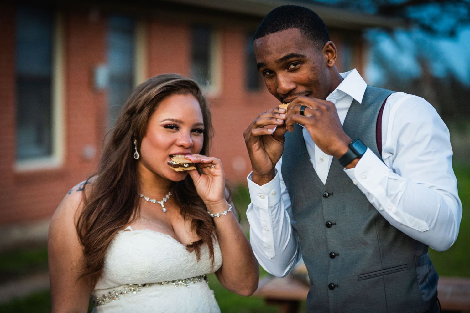 Wedding couple sharing a playful moment while eating something together outdoors.