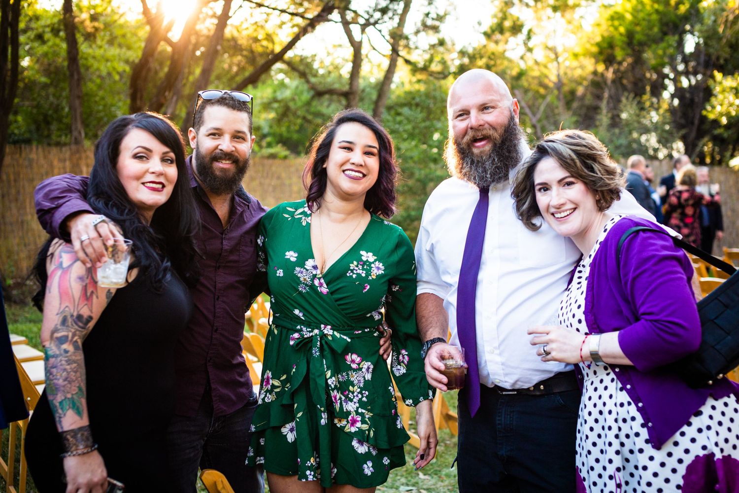 Group of wedding guests in colorful formal attire posing together at outdoor celebration.
