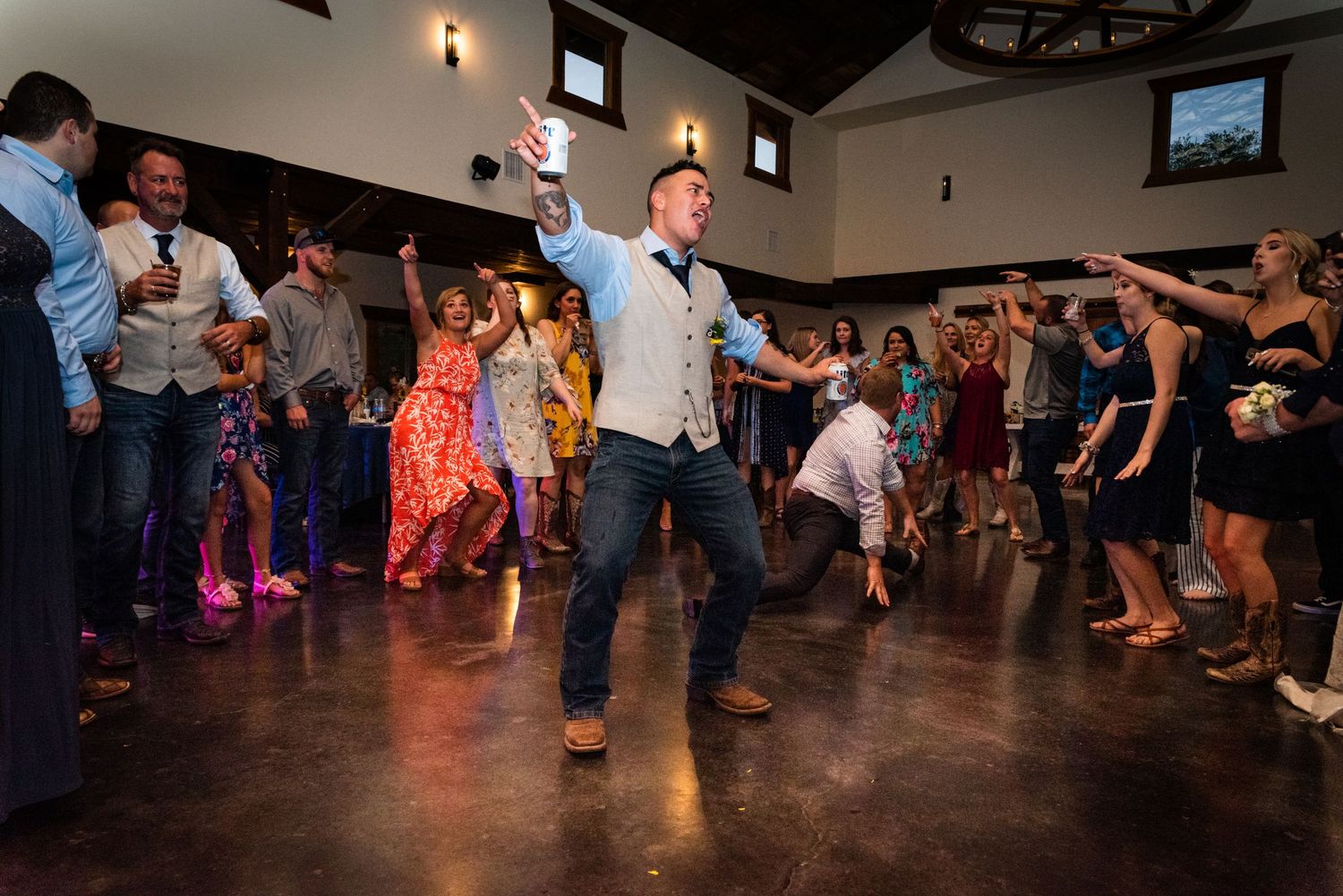 Wedding guests dance and celebrate in a rustic reception venue with wooden decor.