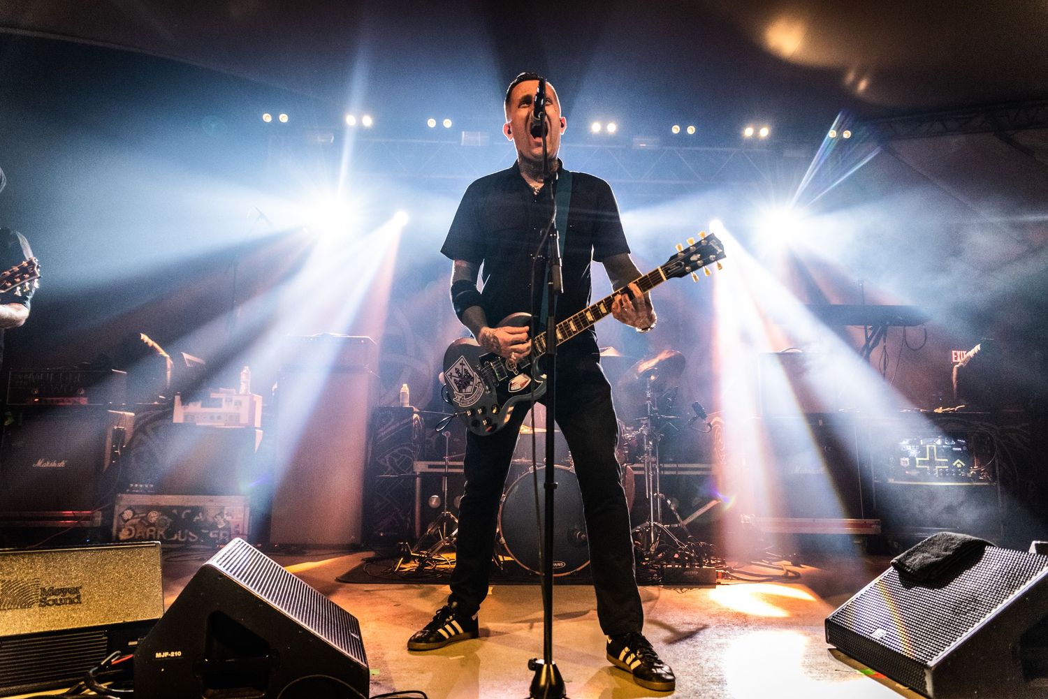 Rock musician performs center stage with dramatic spotlights creating beams in background.