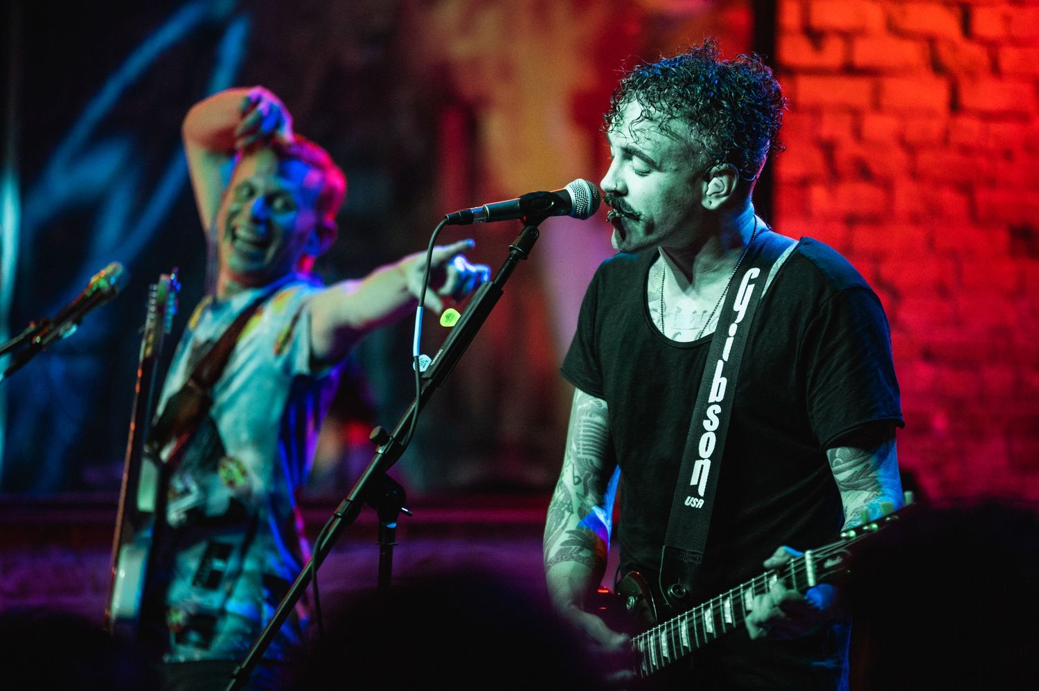 Rock band performing on stage with dramatic lighting and exposed brick wall background.