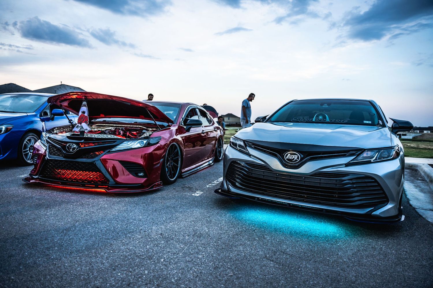 Custom Toyota Camry and modified red sedan with underglow lighting at a car show.
