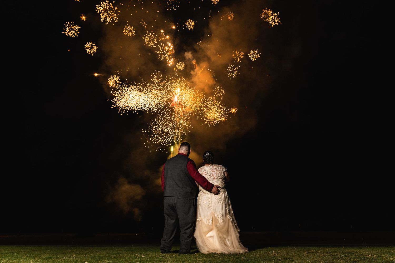 Golden fireworks illuminate the night sky behind a couple watching the display.