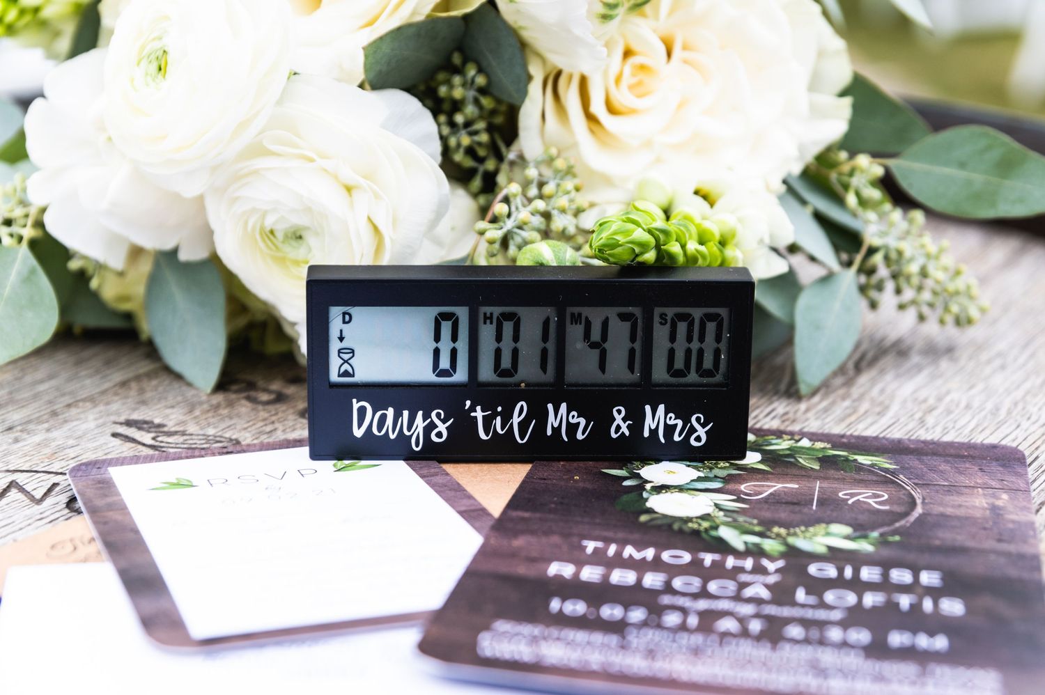 Wedding countdown timer display surrounded by white roses and invitation cards.