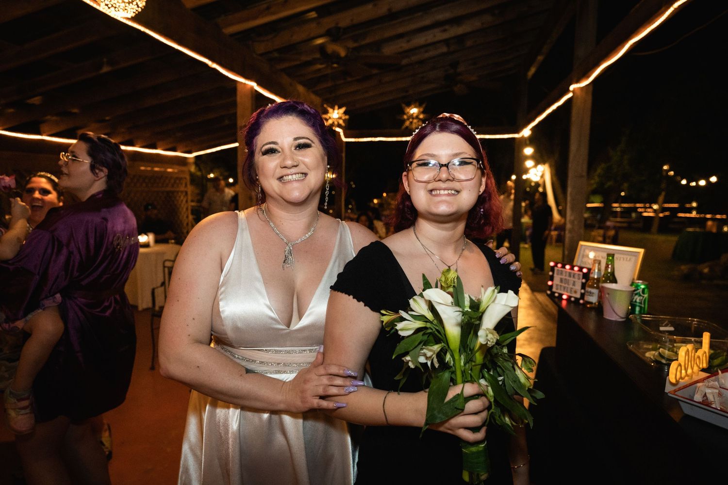 Two guests pose together at an evening reception with string lights in the background.
