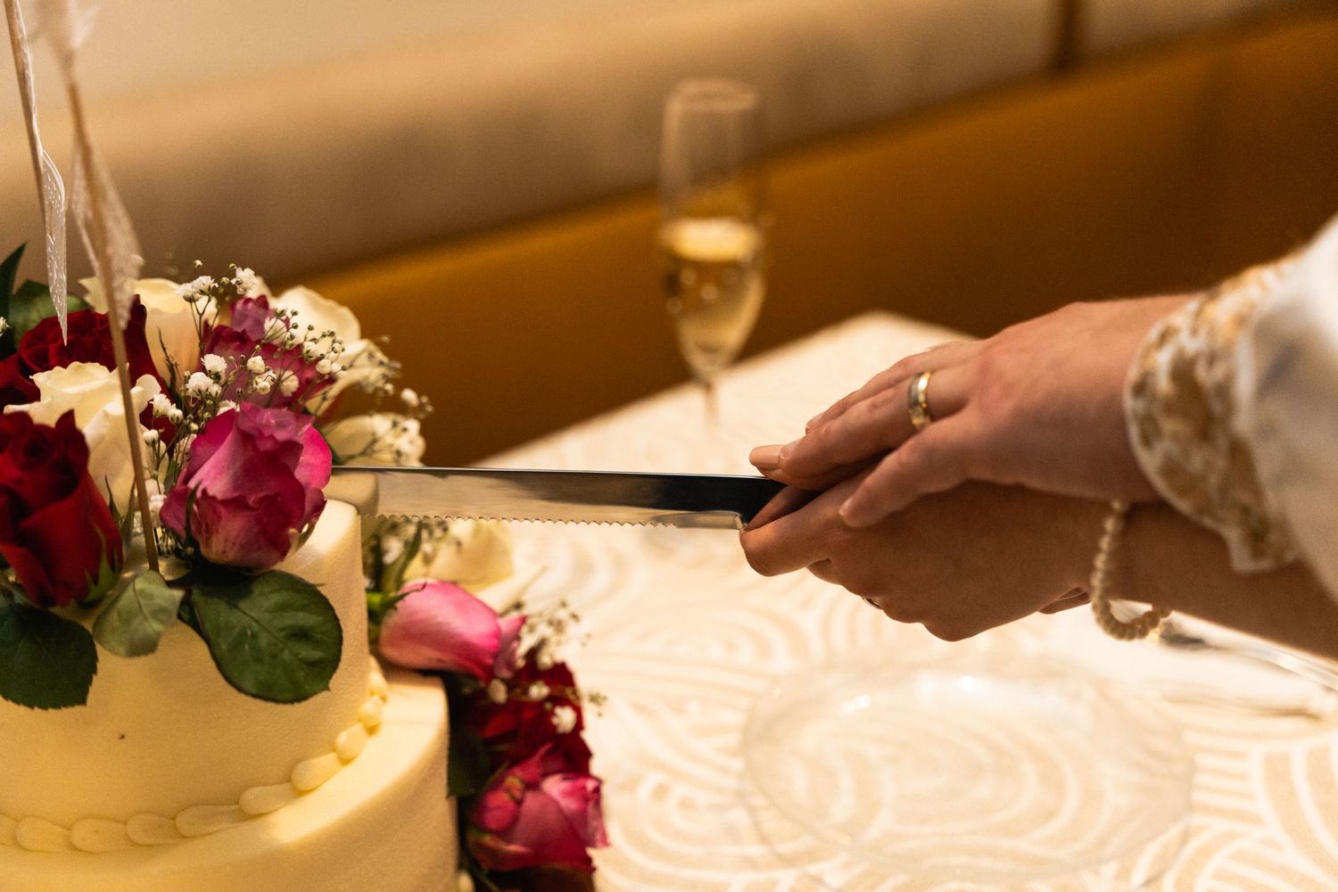 Hand cutting into wedding cake decorated with red and pink roses.