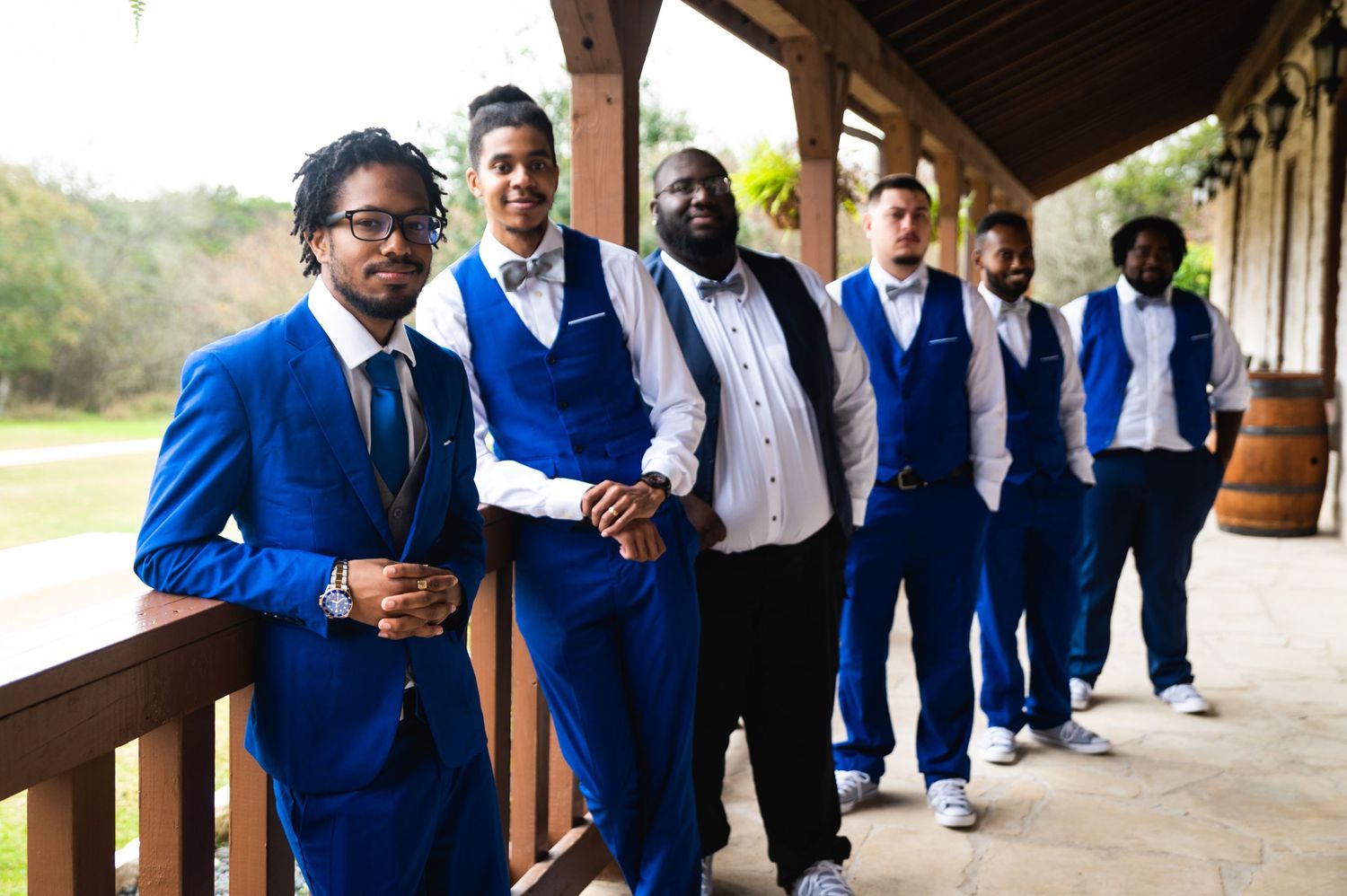 Groomsmen in coordinated royal blue suits pose in a line on a wooden porch.