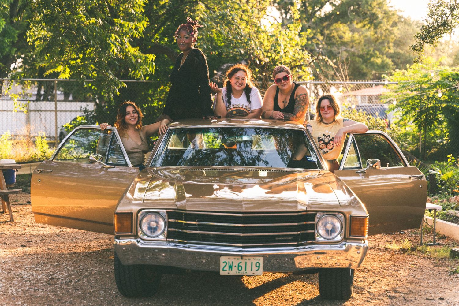 Group of friends posing on top of a vintage Chevrolet car during golden hour.