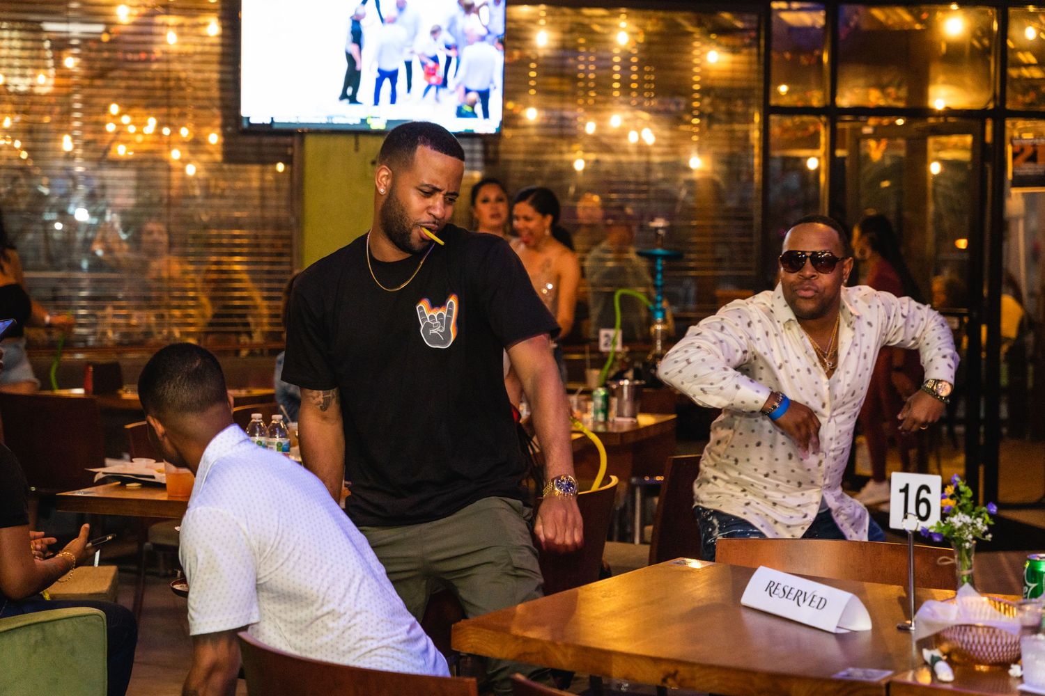 Group of friends hanging out at a casual restaurant with a TV screen in the background.
