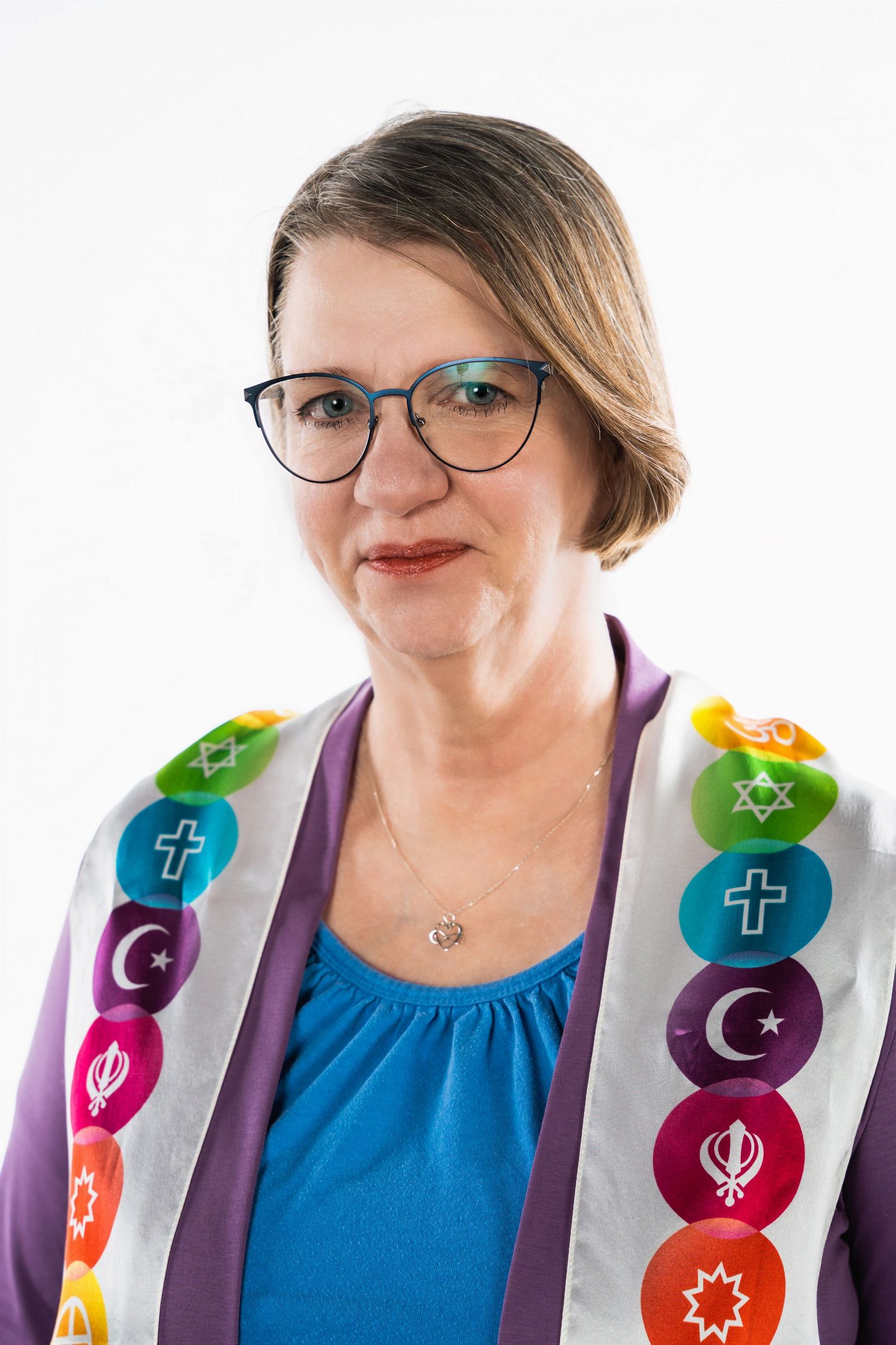 Person wearing interfaith stole with religious symbols over blue top and purple cardigan.