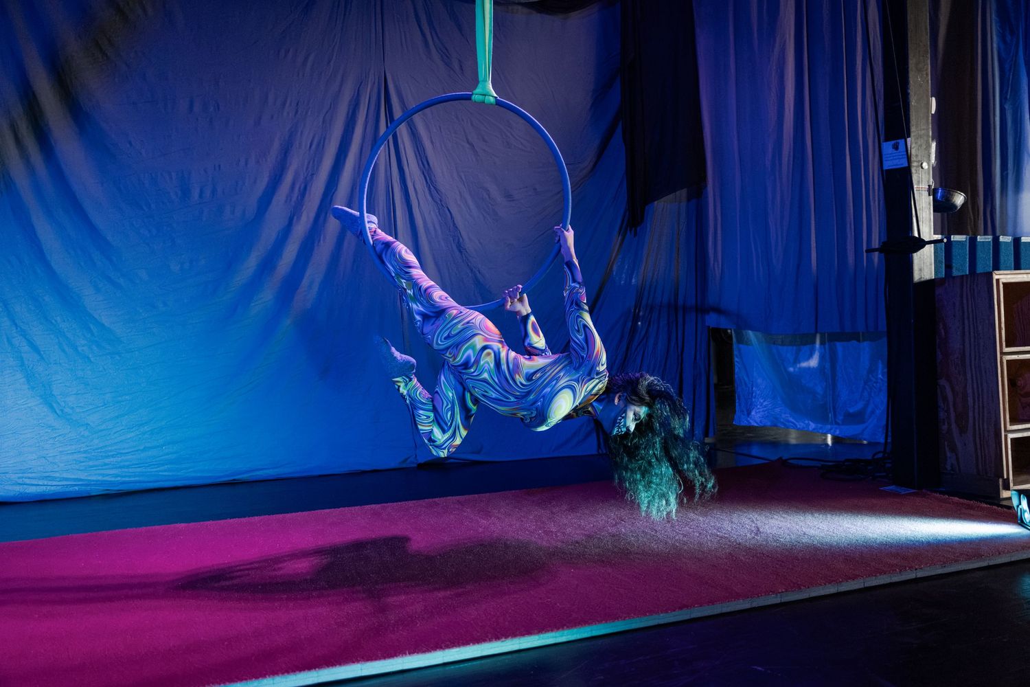 Aerial acrobat performing on a hoop in a dramatic blue-lit circus stage setting.