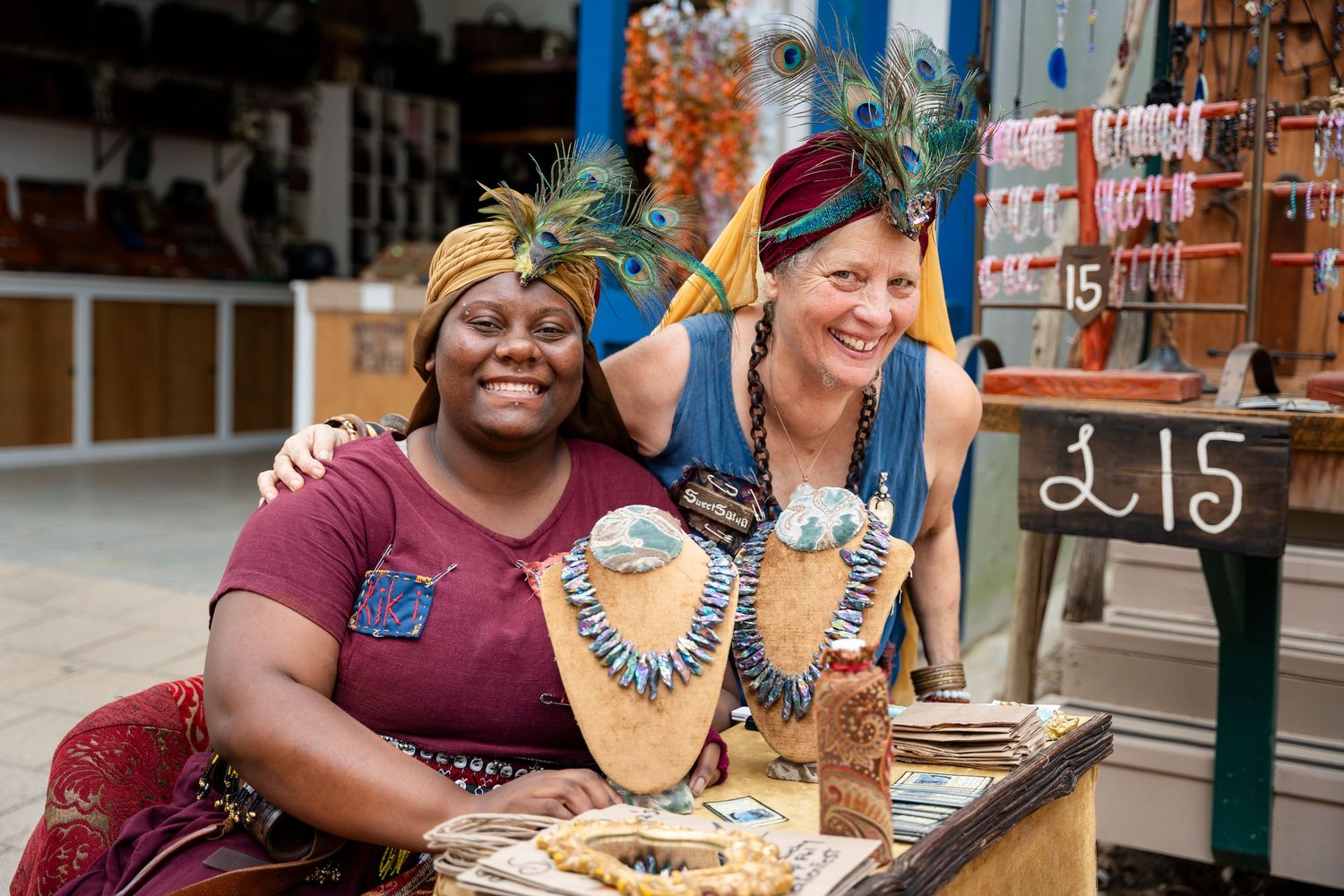 Two friends share a joyful moment while looking at jewelry displayed at a market stall.