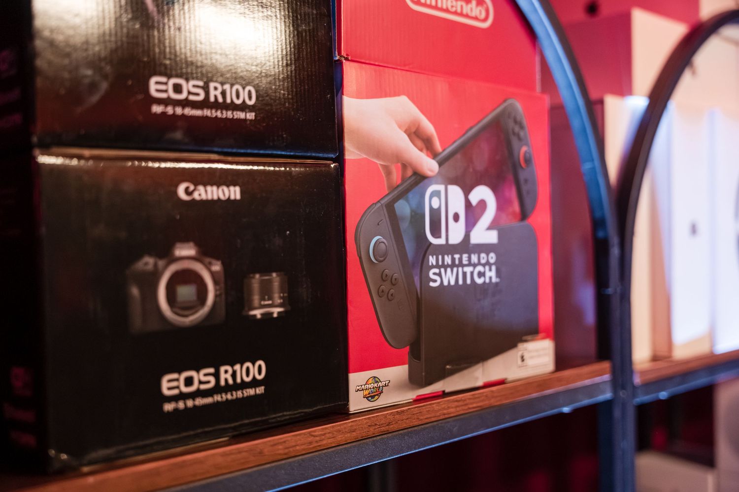 Canon EOS R100 camera and other photography equipment displayed on retail store shelves.