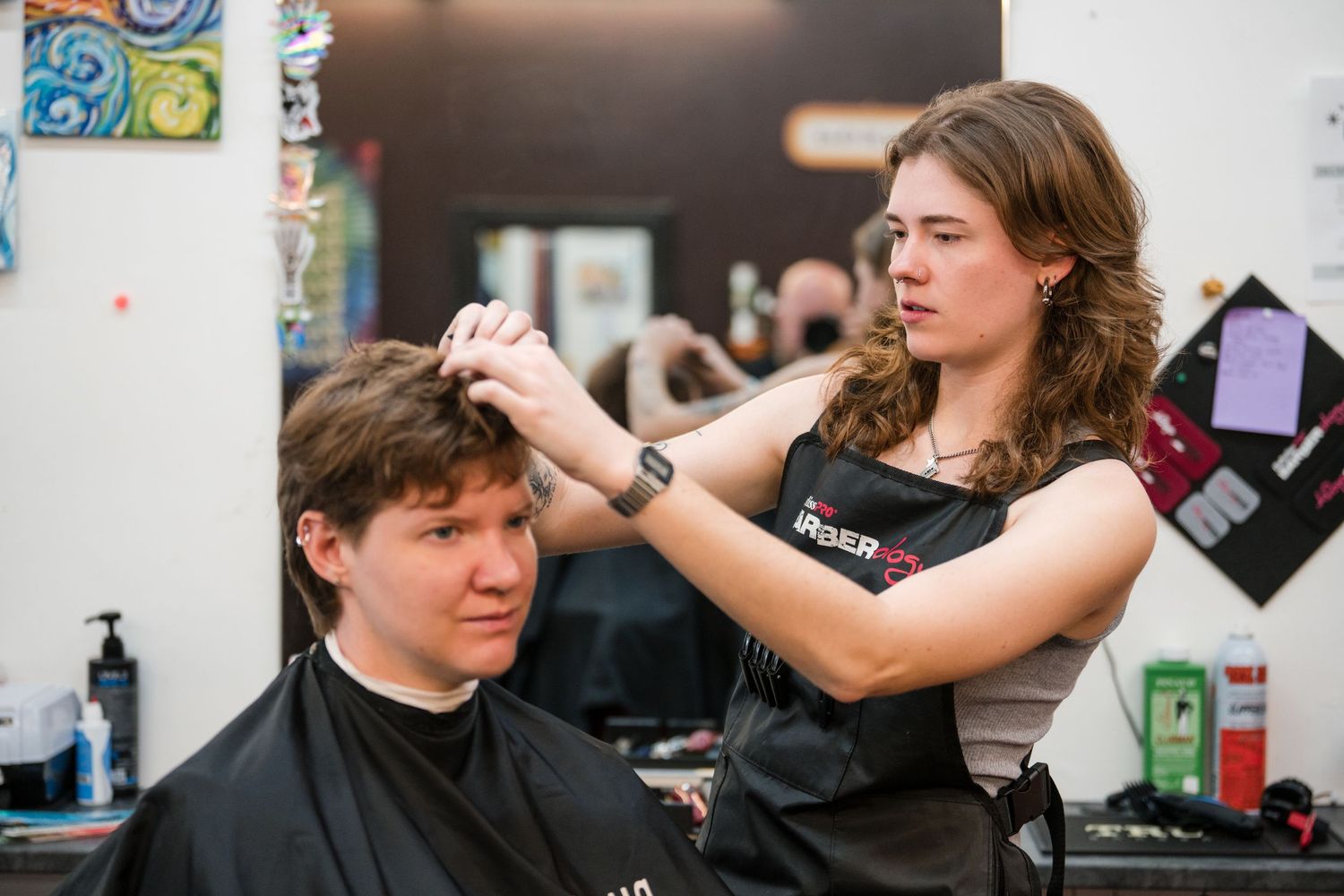 A hairstylist wearing a black apron styles a client's hair in a modern salon setting.