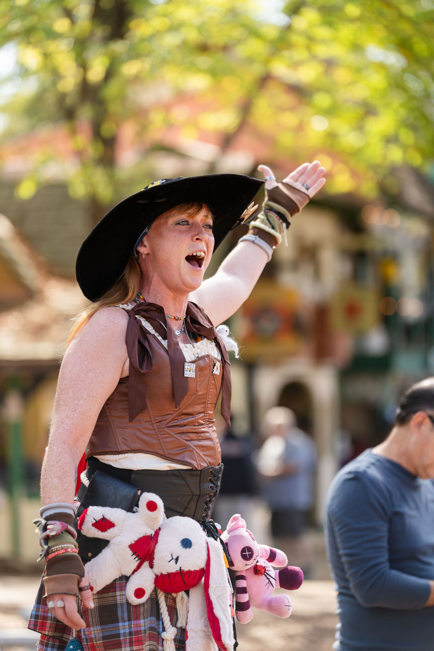 Person in western attire rides a toy stick horse while performing at an outdoor event.