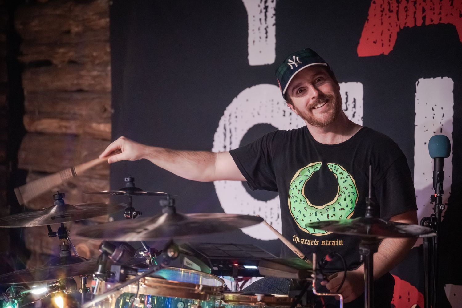 A drummer performs on stage with dynamic lighting and multiple camera angles showing their energetic performance.