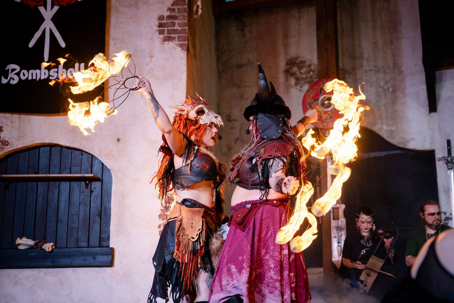 Fire performers demonstrate dangerous fire breathing tricks in a dark indoor space with brick walls.