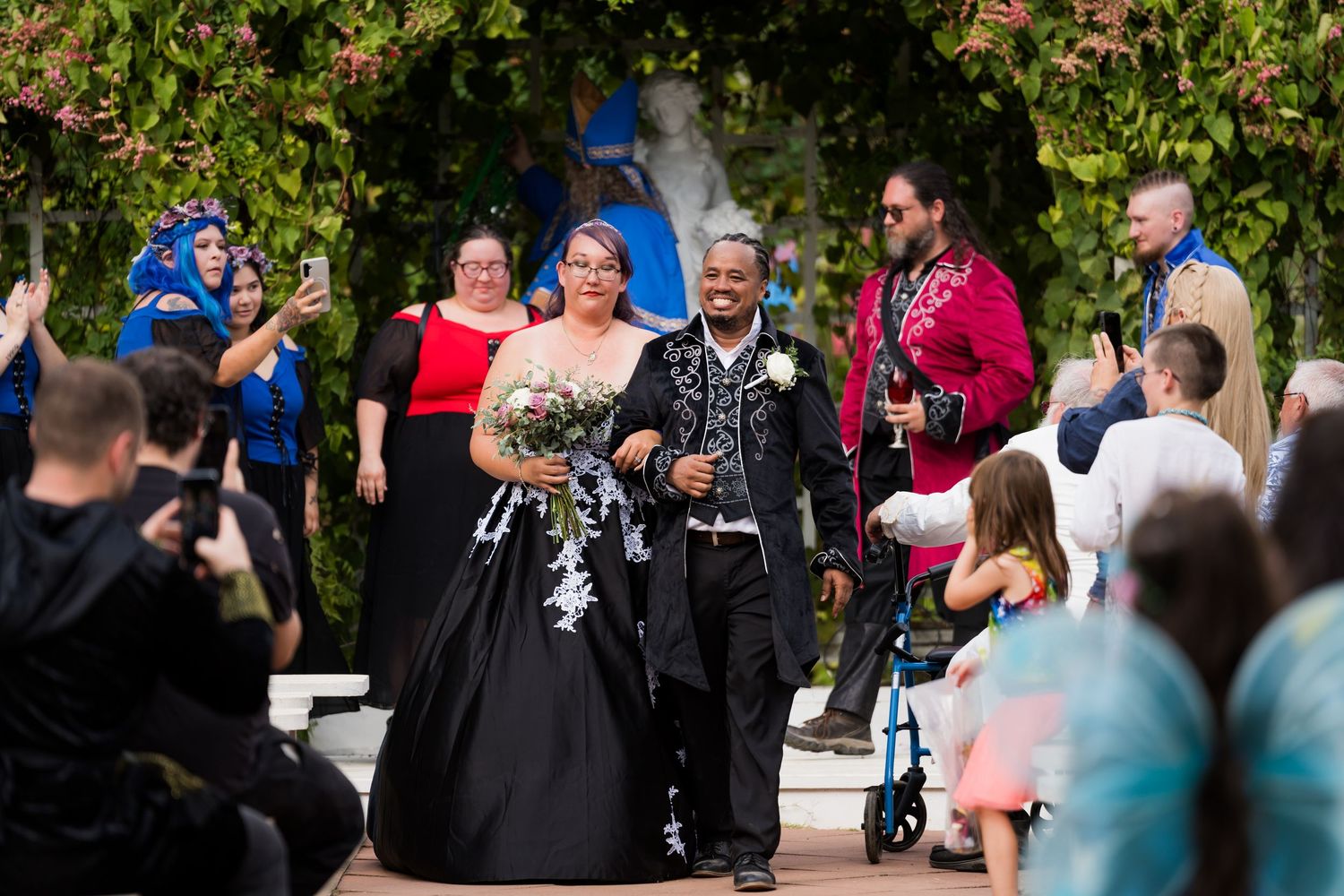 A group of wedding guests gather outdoors in a garden setting during a celebratory moment.