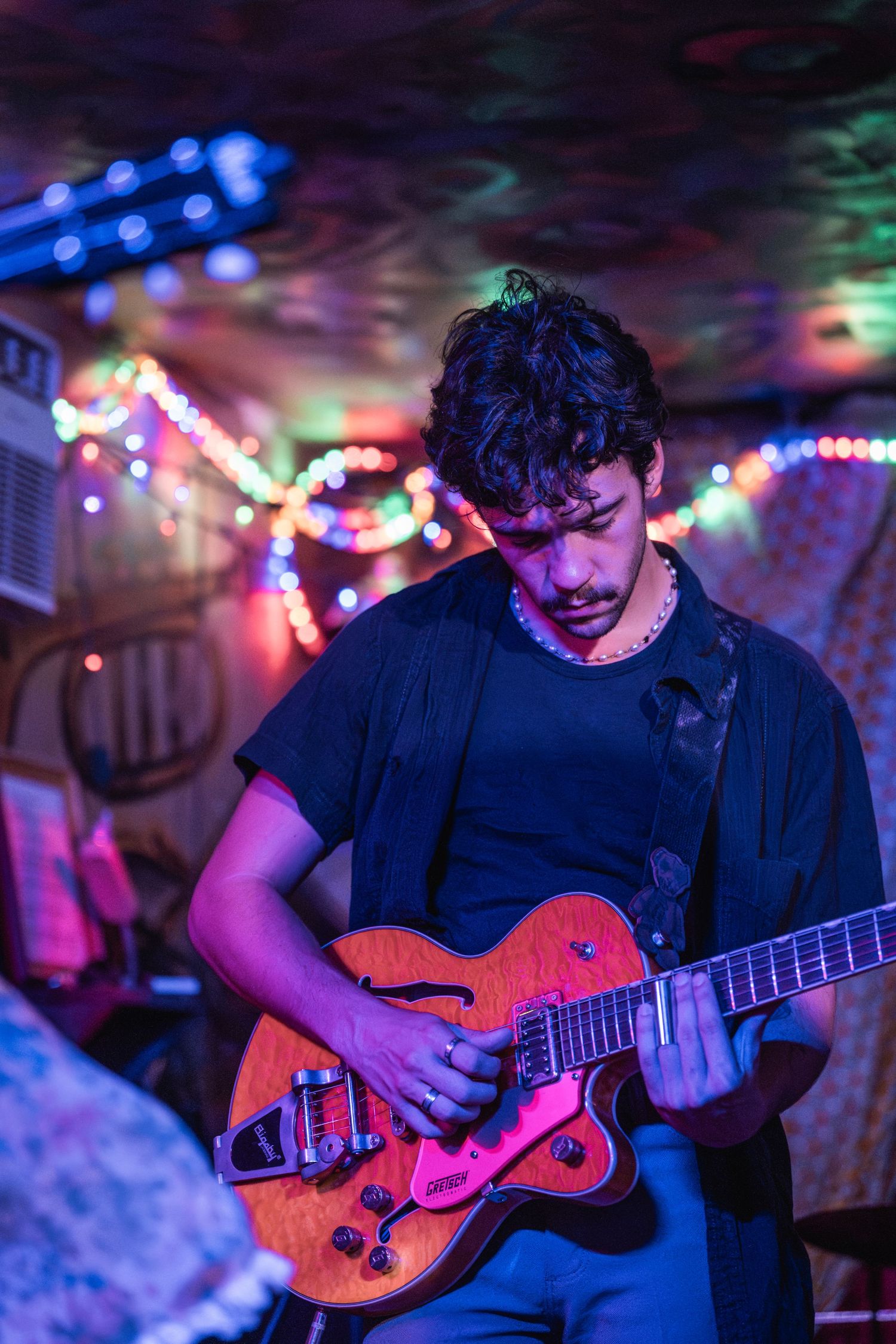 Guitarist performs on stage with colorful string lights creating a vibrant atmosphere in the background.