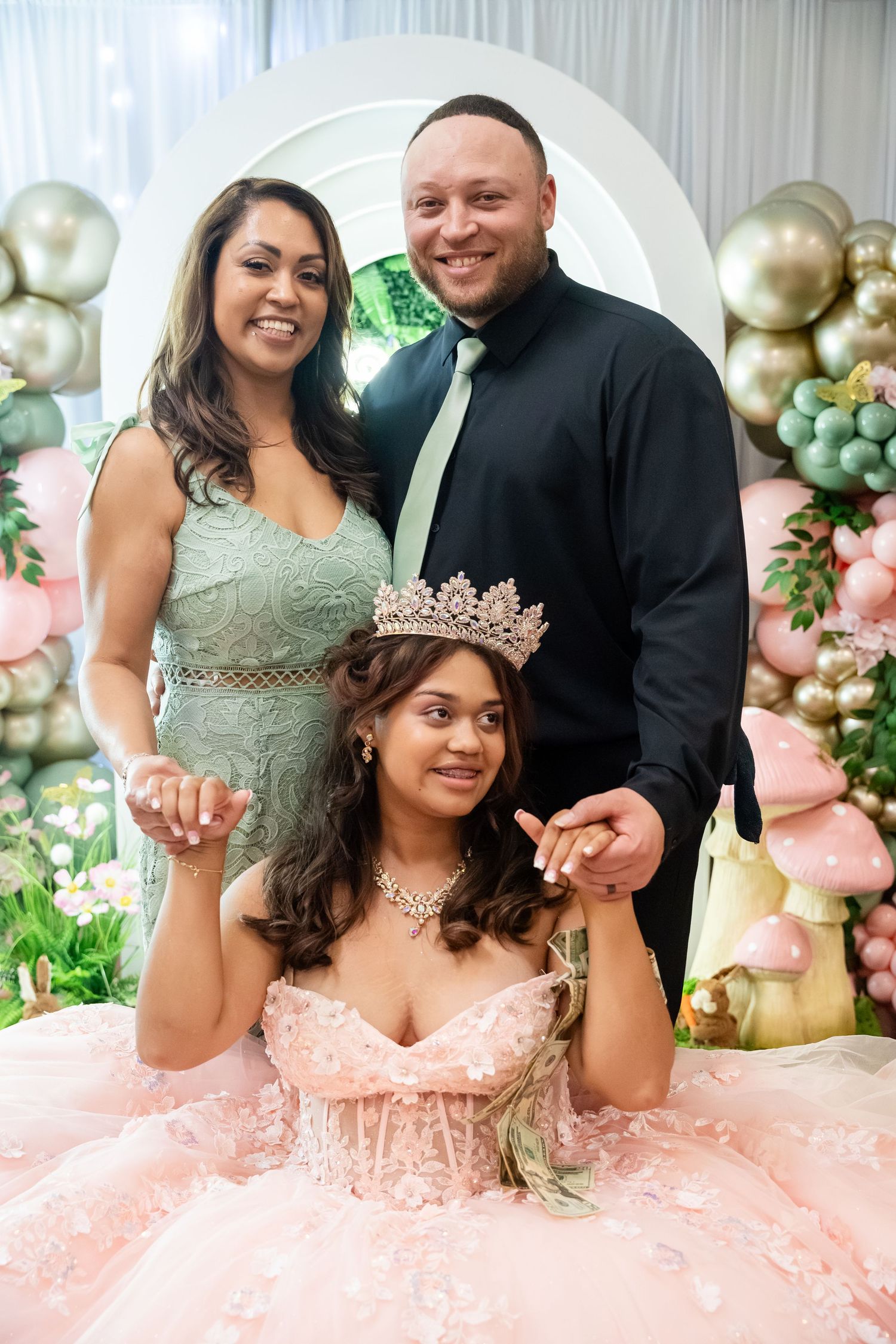 Family posing at a quinceañera with parents standing behind their daughter wearing a pink ball gown and tiara.