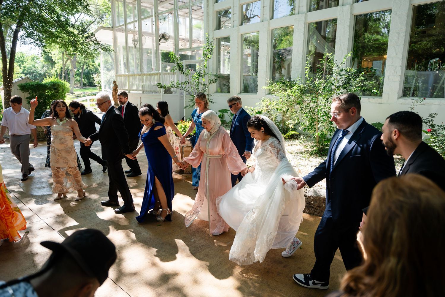 Bride in white gown dances with guests in elegant outdoor wedding celebration at a sunlit venue.