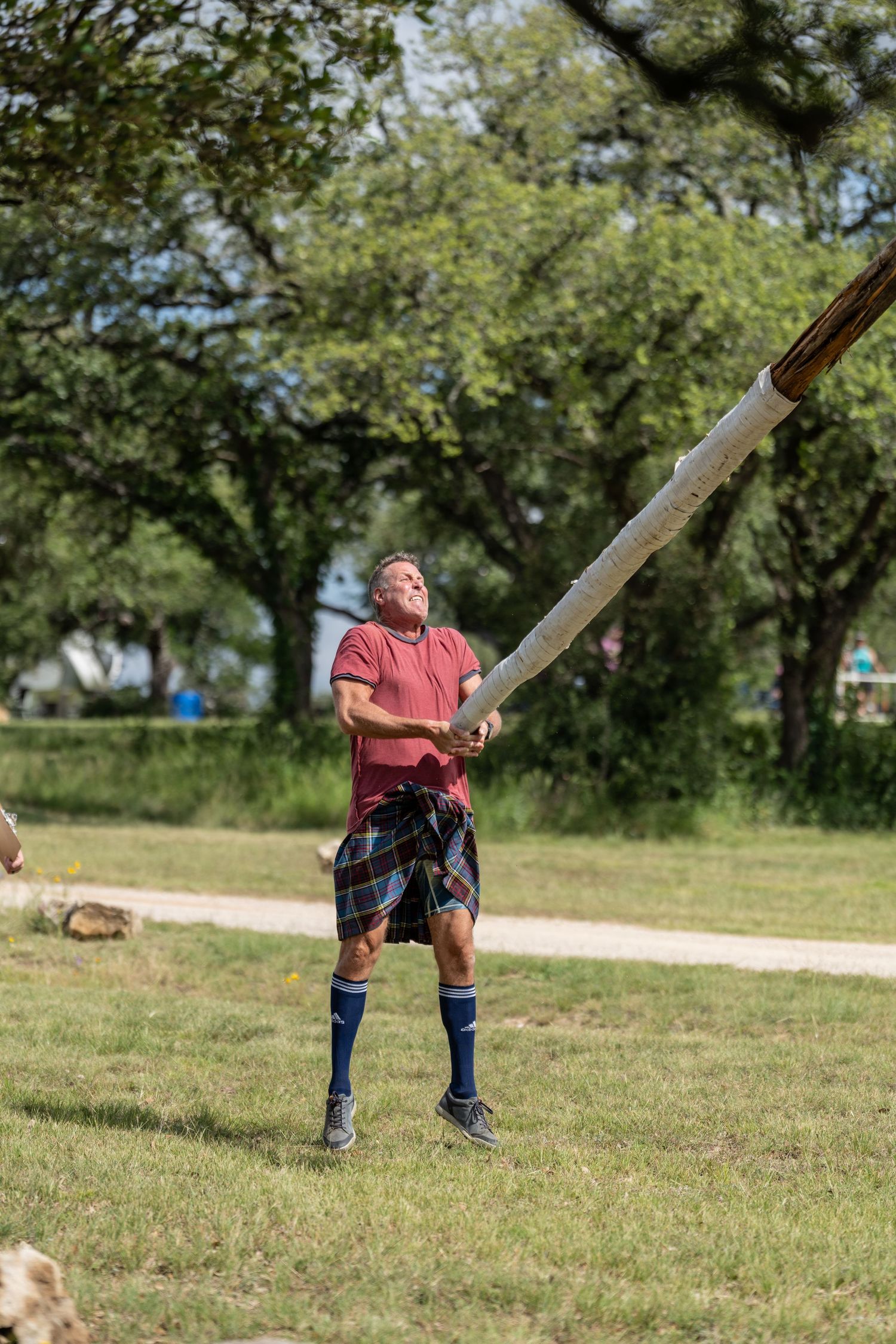Man in tartan kilt tossing a caber at a Highland Games competition outdoors.