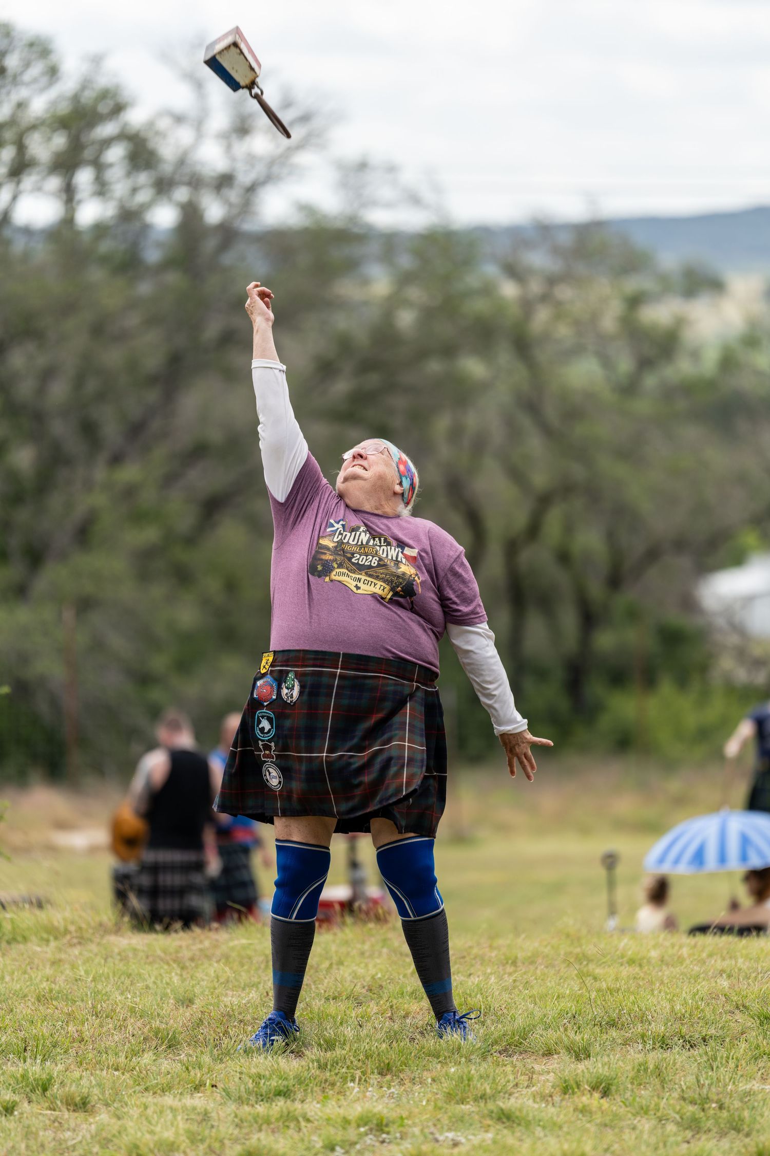 Man in tartan kilt throwing weight at Scottish Highland Games competition outdoors.