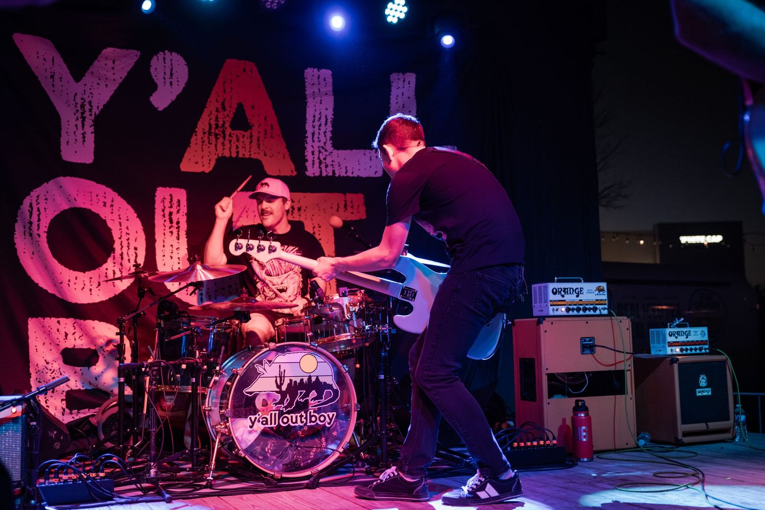 Two musicians perform energetically on stage beneath a bold pink Y'all Quiet Down sign at a live concert.