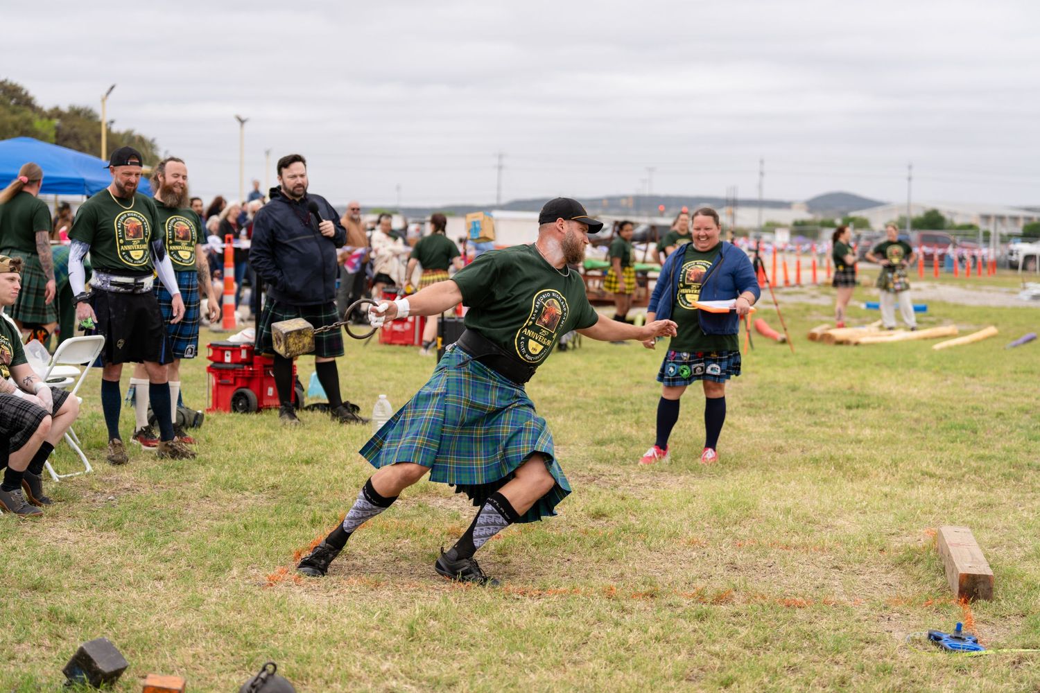Man in tartan kilt competing at Highland Games event, surrounded by spectators on a grassy field.