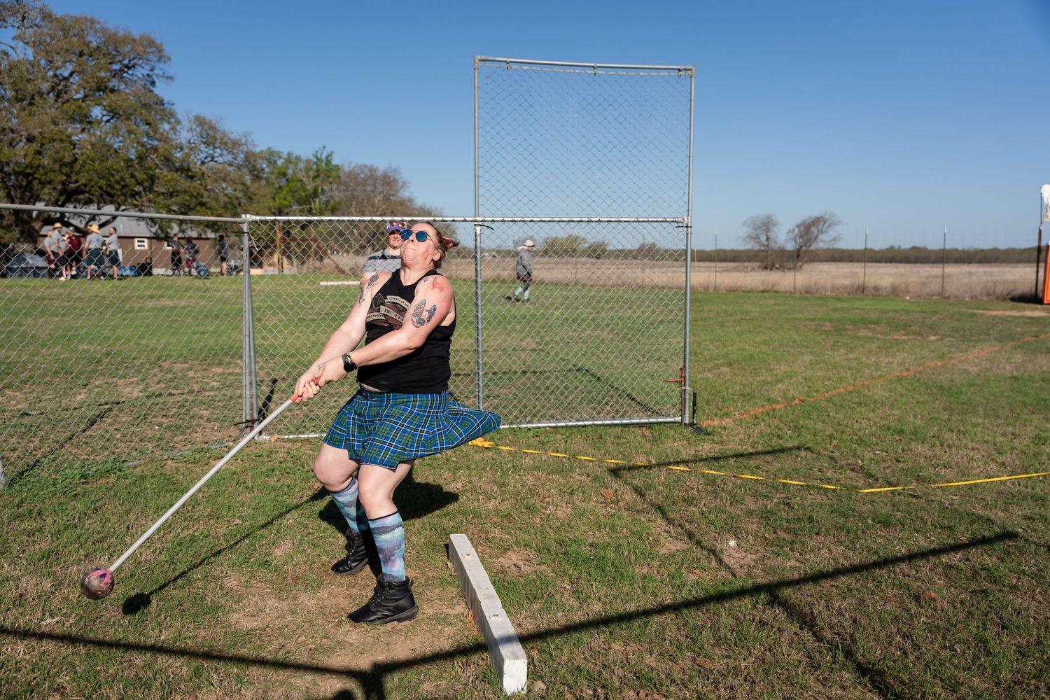Man in kilt competing in Highland Games hammer throw event outdoors on a sunny day.