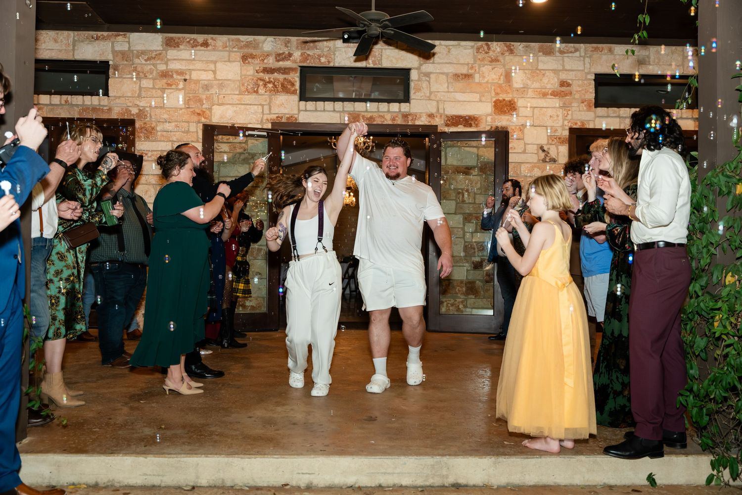 Newlywed couple celebrates grand exit at wedding reception surrounded by cheering guests in elegant venue.